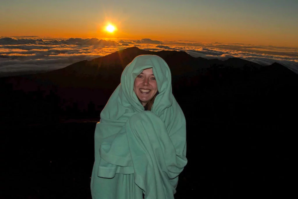 Person wrapped in a blanket watching sunrise at Haleakala