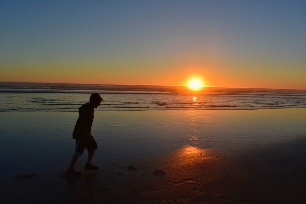 boy walking on beach at sunset